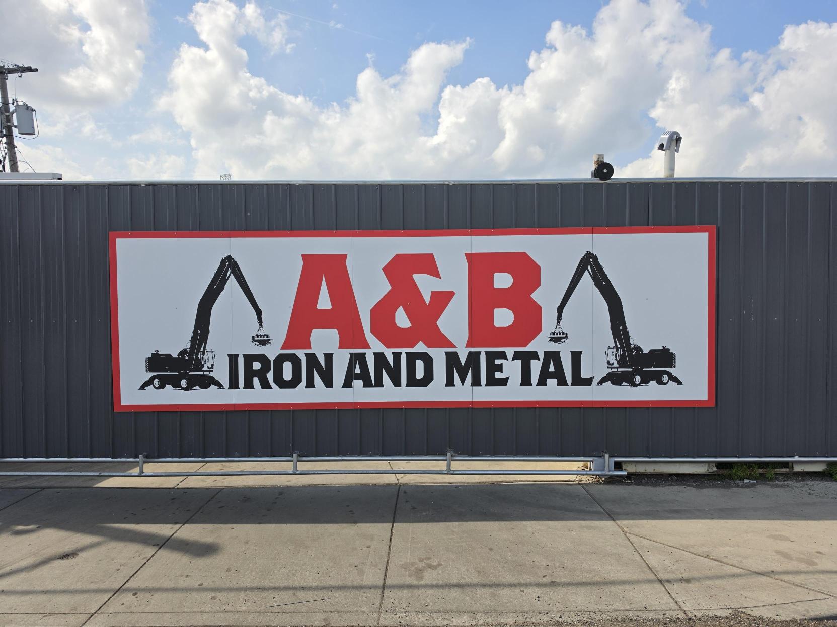 The red and white A&B Iron and Metal sign, flanked by two material handlers, on the grey wall of the Dayton yard